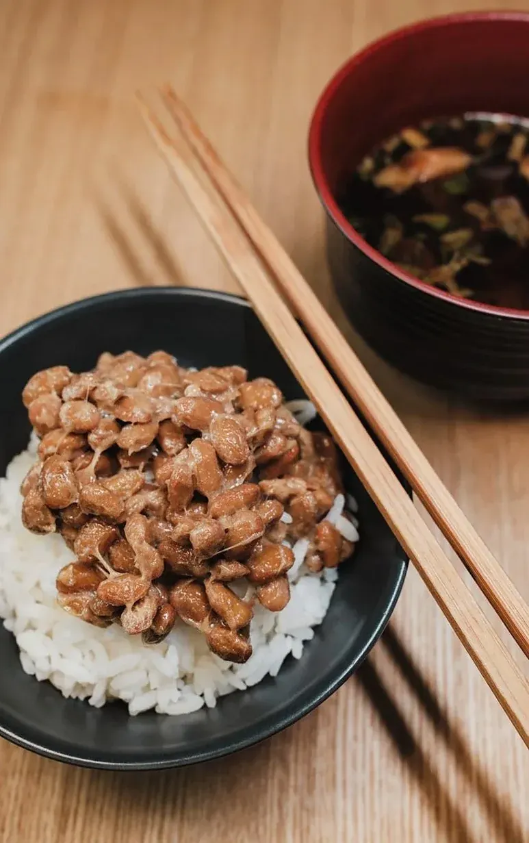 木のテーブルに置かれた、納豆をのせたご飯と味噌汁と箸（イメージ写真）
